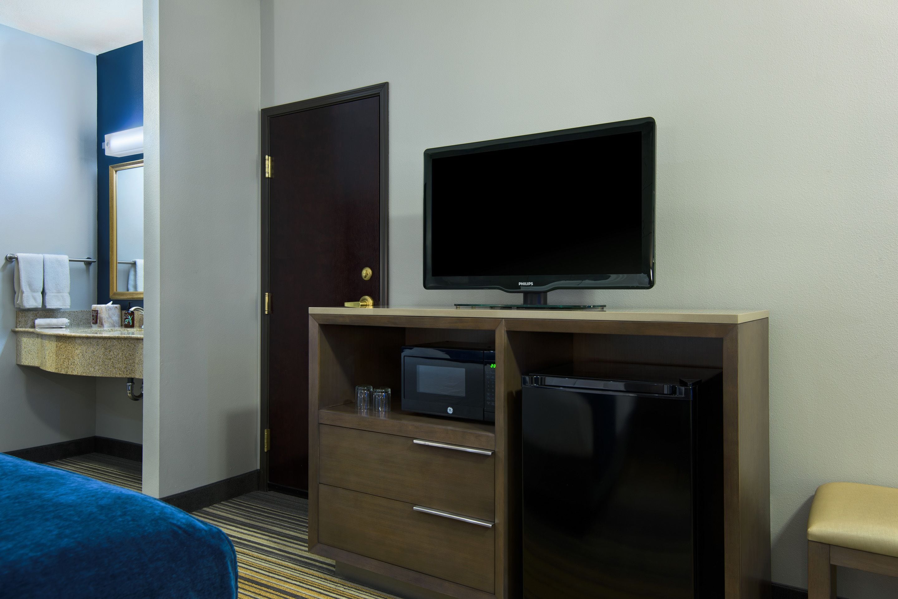 A hotel room with a bed, a desk with a television, a refrigerator, a microwave, and a mirror.