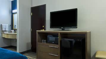 A hotel room with a bed, a desk with a television, a refrigerator, a microwave, and a mirror.