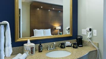 A hotel bathroom with a sink, mirror, towel rack, toiletries, and a hairdryer.