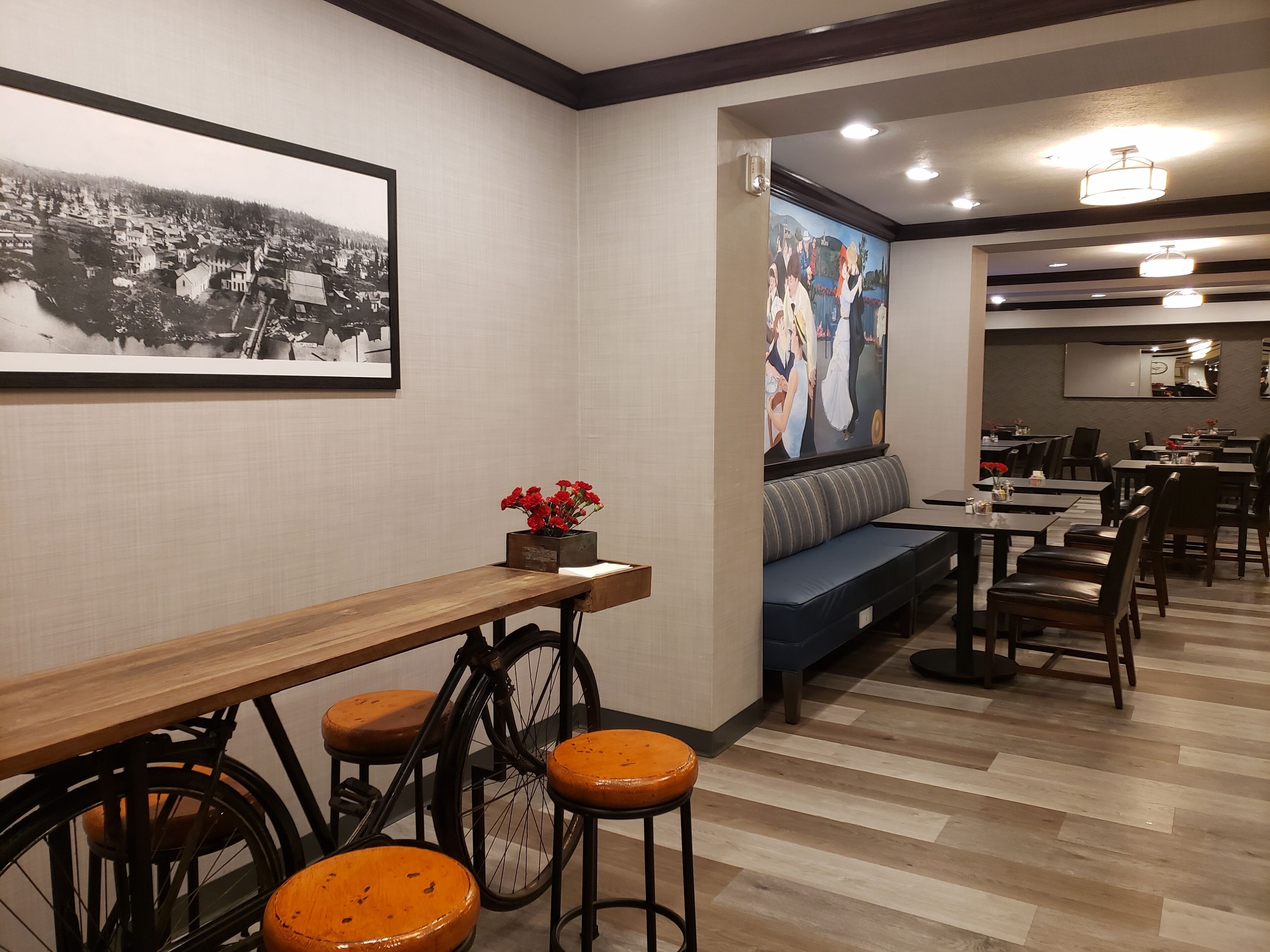 A restaurant interior with a wooden bar, stools, a seating area with a sofa, and a mural on the wall.