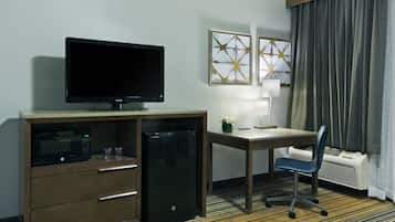 Een hotelkamer met een bureau, een televisie, een magnetron, een minibar, een stoel en twee ingelijste kunstwerken aan de muur.