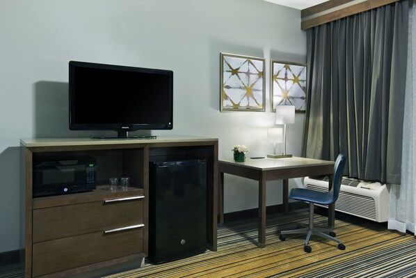 A hotel room with a desk, a television, a microwave, a mini-fridge, a chair, and two framed artworks on the wall. - Oxford Suites Downtown Spokane (Spokane)