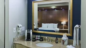 Een hotelbadkamer met een grote spiegel, een wastafel, een haardroger, een koffiezetapparaat en toiletartikelen.