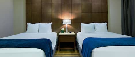 A hotel room with two beds, a nightstand with a lamp, and a striped carpet.