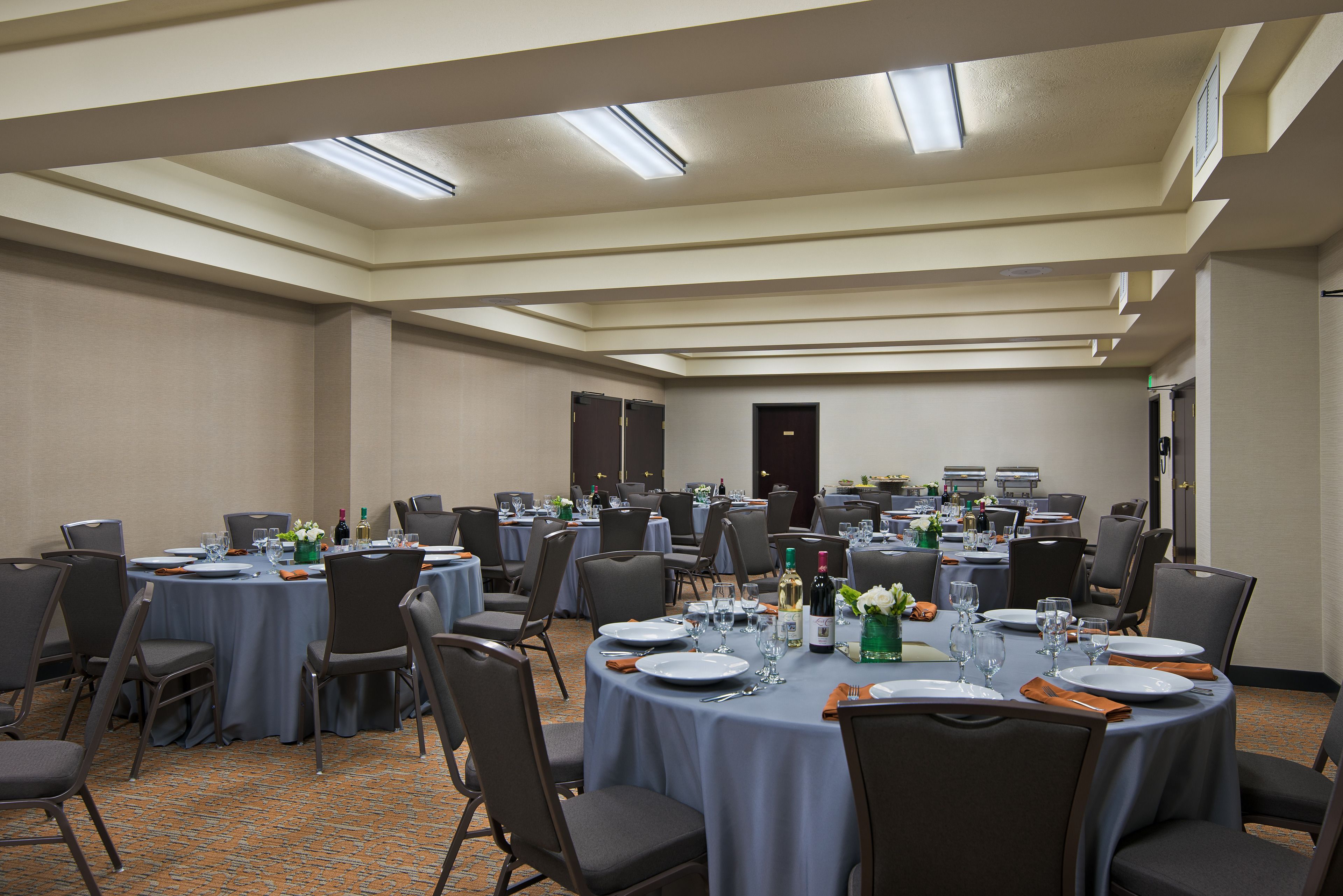 A conference room with multiple tables set for dining, equipped with chairs, plates, cutlery, and wine bottles.