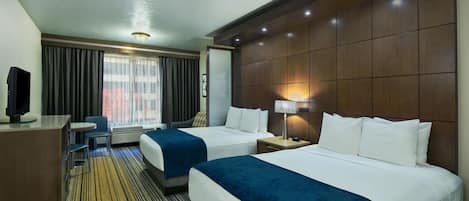 A hotel room with two beds, a desk, a chair, and a TV.