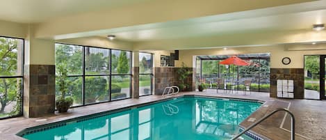 Une piscine intérieure avec des parois en verre transparent, une terrasse carrelée et une vue sur l’extérieur.