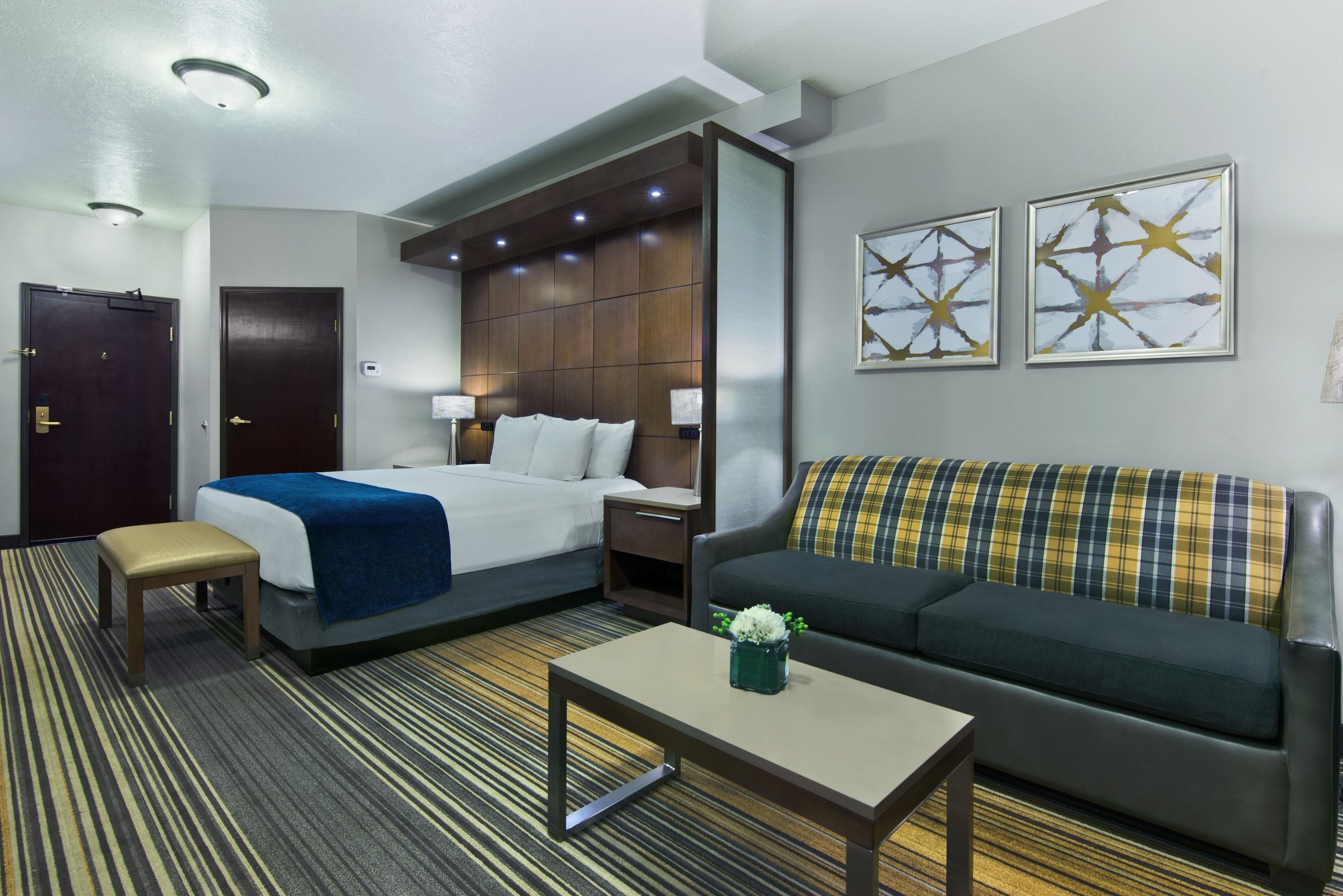 Habitación de hotel con una cama, un sofá, una mesita, un banco y dos lámparas fijadas a la pared.