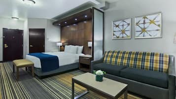 Habitación de hotel con una cama, un sofá, una mesita, un banco y dos lámparas fijadas a la pared.