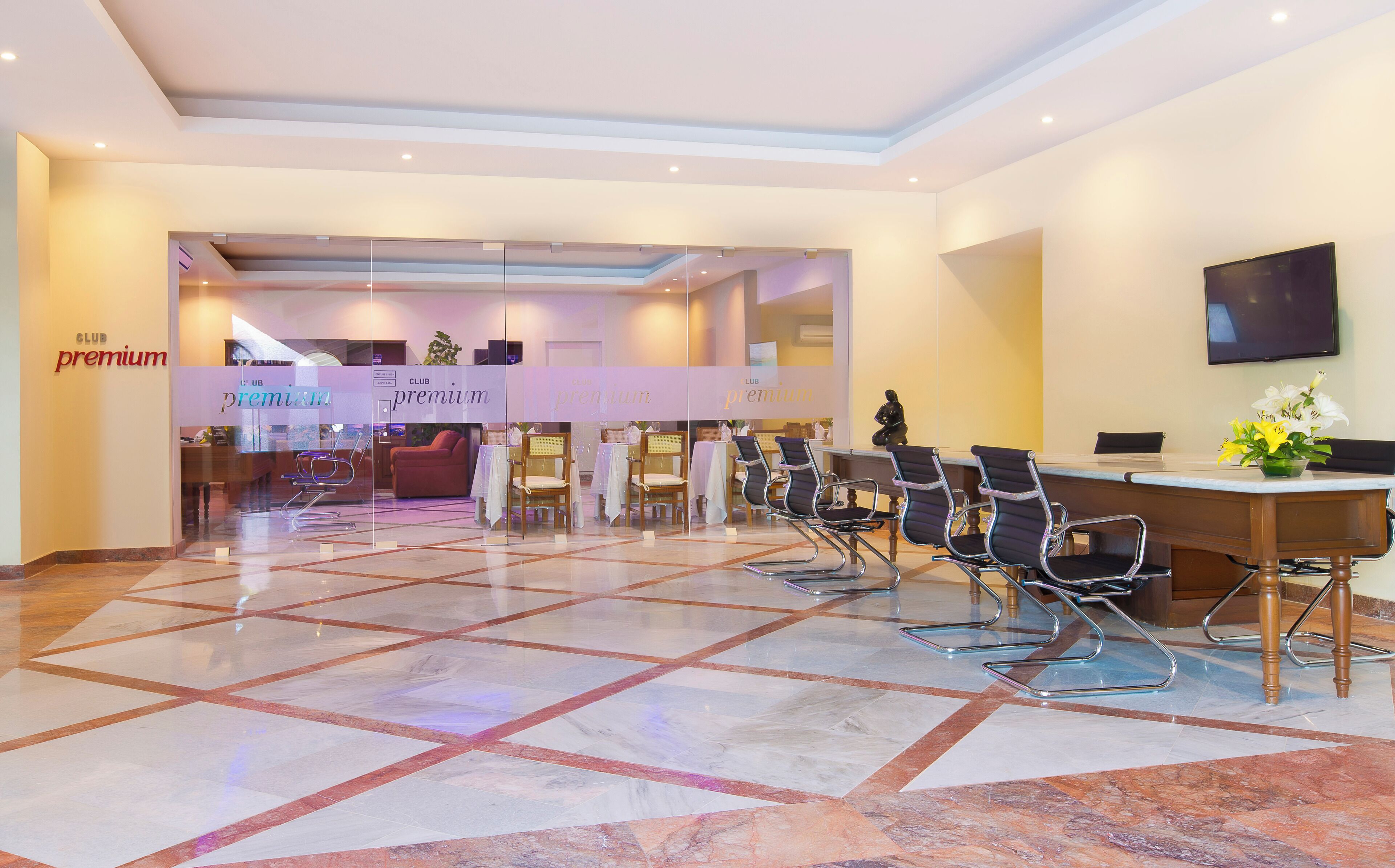 A hotel lobby with a reception desk, several chairs, a television, and a tiled floor.