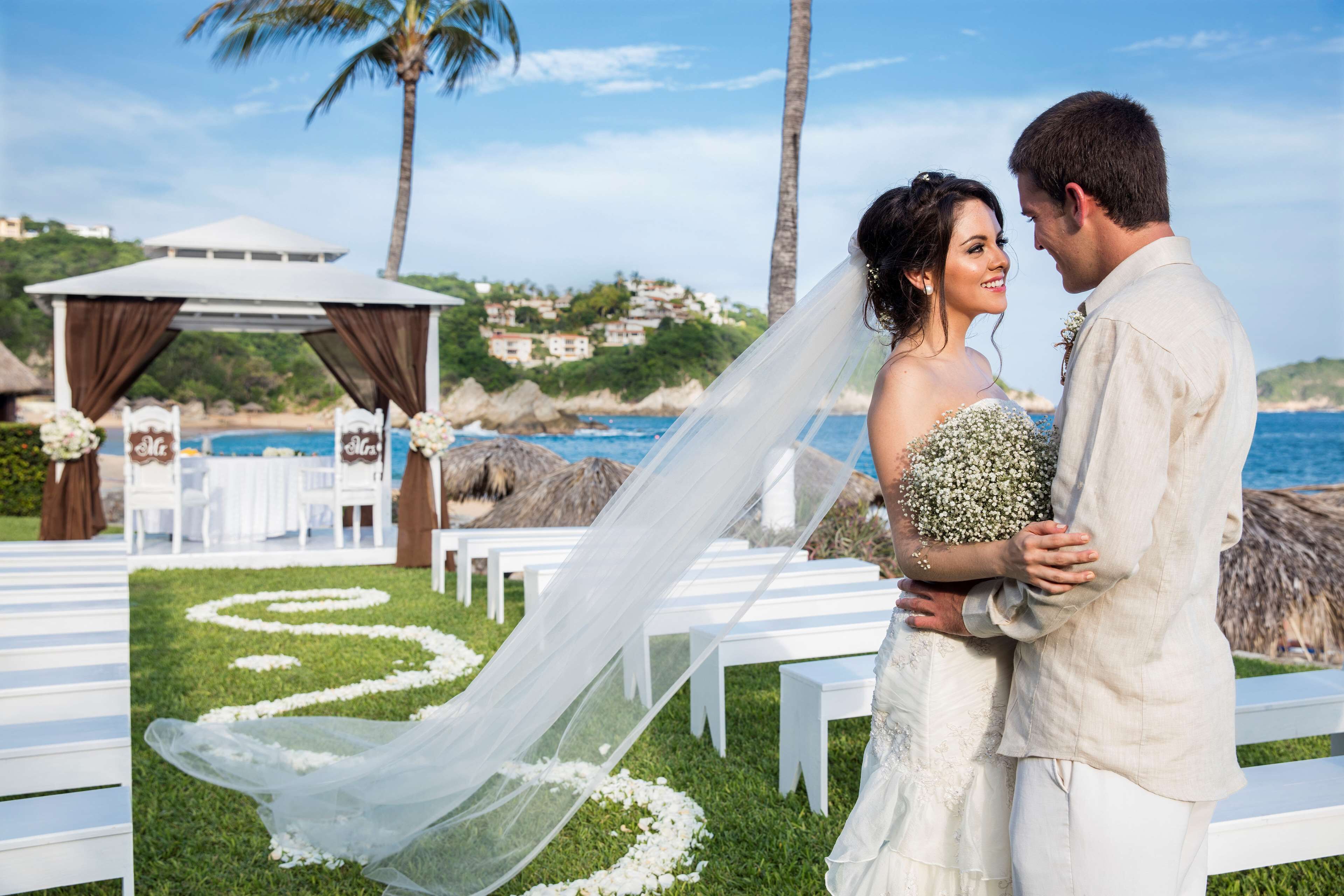 A wedding ceremony with a white aisle, white chairs, and a tent with drapes.