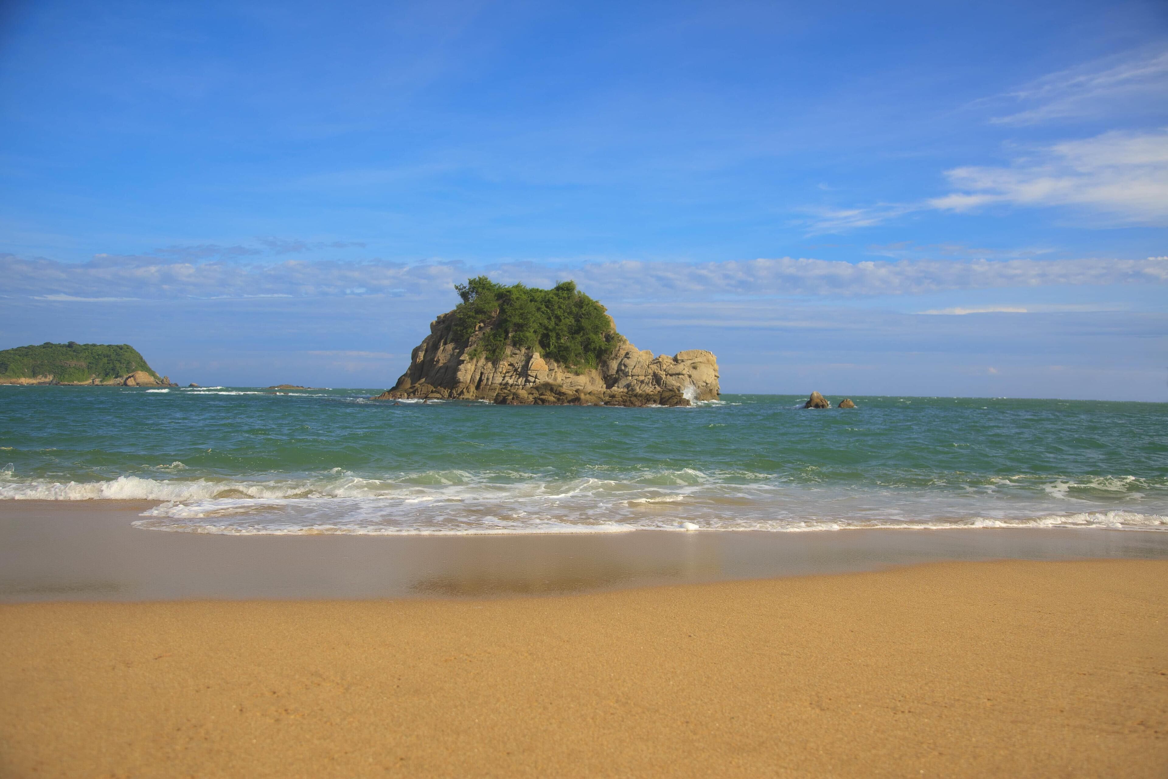 Una playa con una isla rocosa y mar tranquilo.