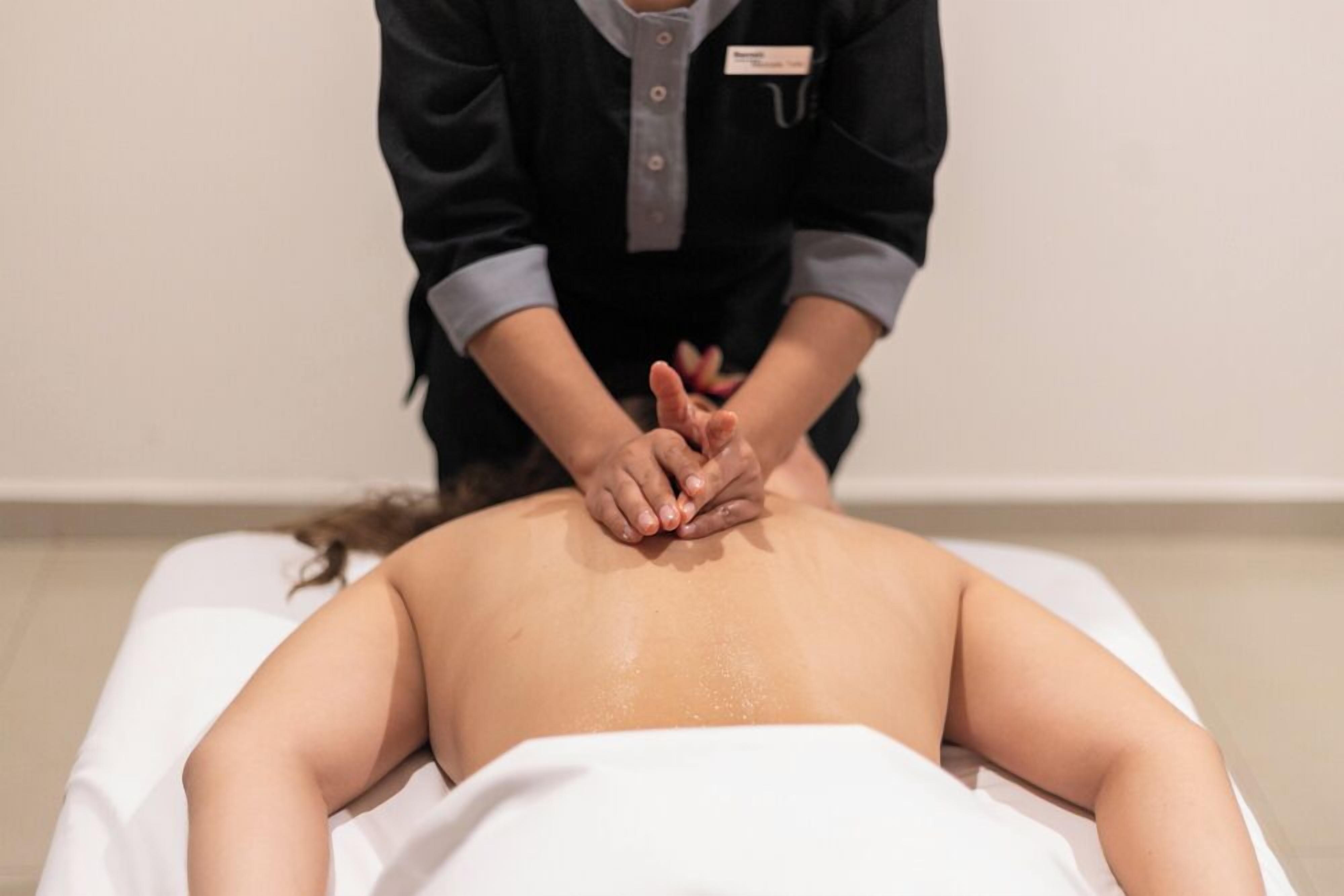 A person receiving a back massage on a white massage table in a room with plain walls.