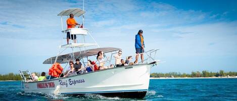 A boat named 'Reef Express' with passengers and a crew member standing on the deck.