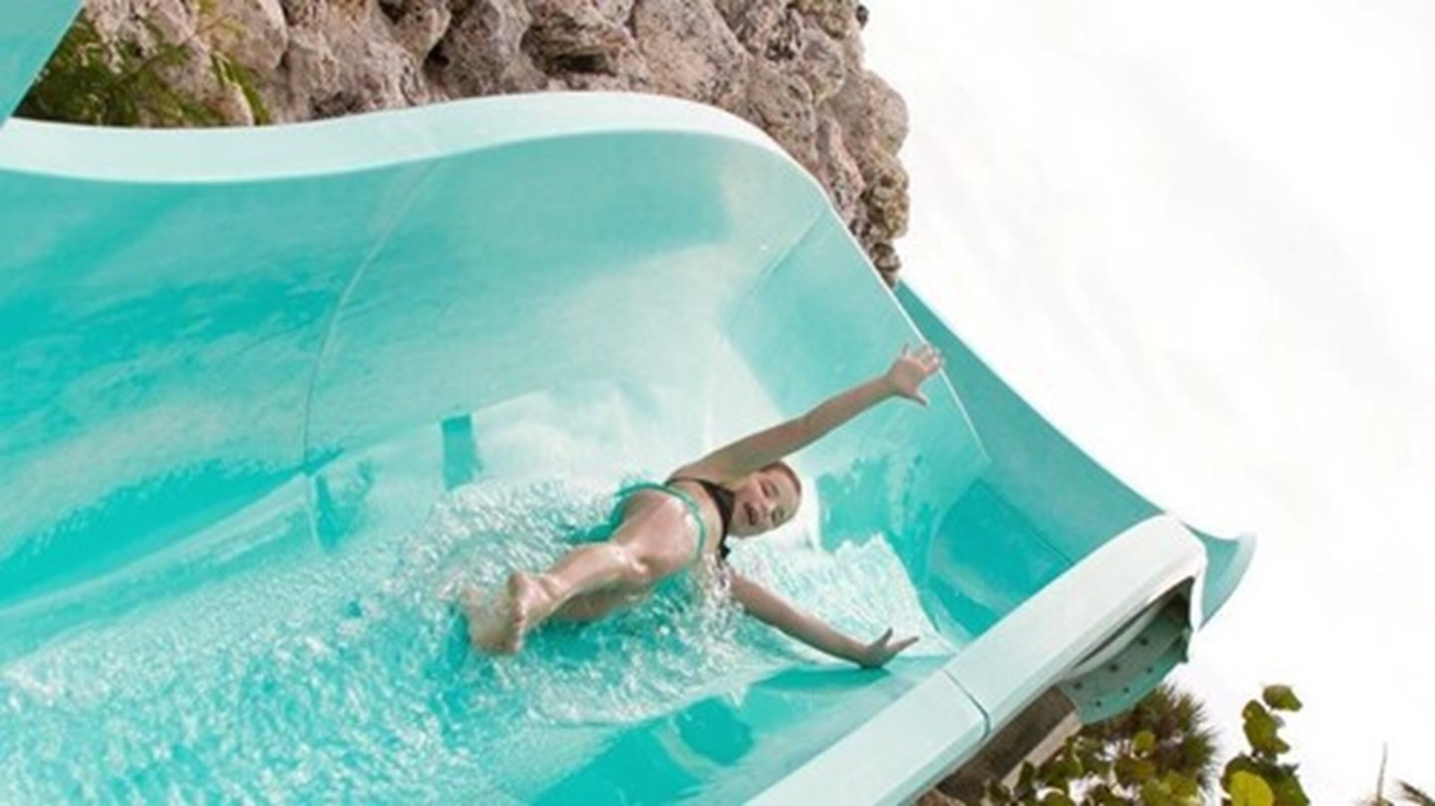 A person in a swimsuit sliding down a clear water slide.