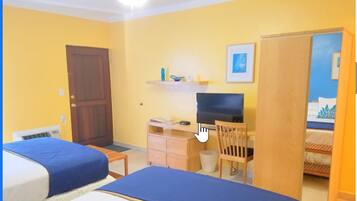 Een hotelkamer met twee bedden, een bureau met een computer, een stoel, een televisie en een deur die naar een andere kamer leidt.