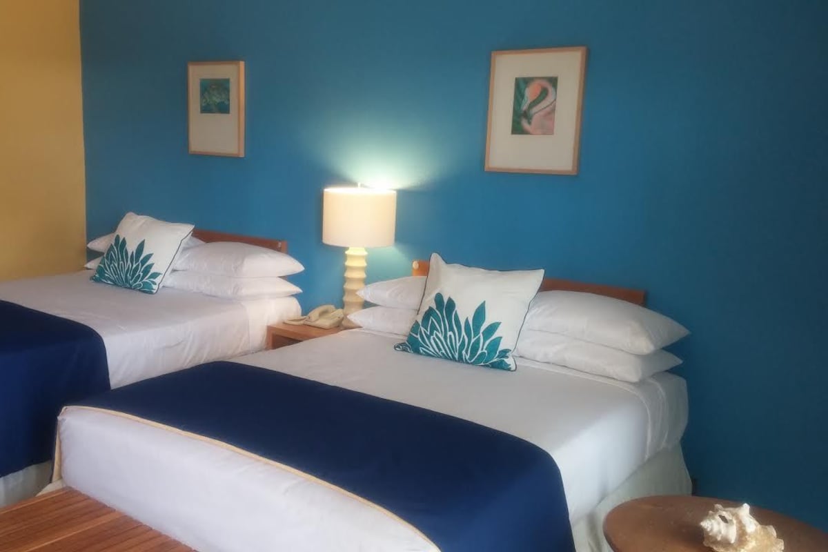 Una habitación de hotel con dos camas, una mesita de noche y una lámpara, y una puerta.