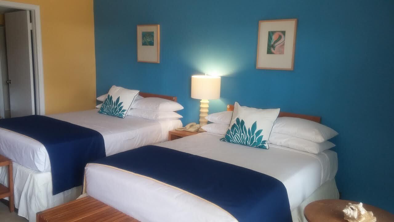 Een hotelkamer met twee bedden, een nachtkastje, een lamp en kunst aan de muren.