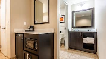 Une salle de bain moderne avec un lavabo intégré, un grand miroir, un four à micro-ondes et un meuble en bois foncé doté d’une étagère pour les serviettes.