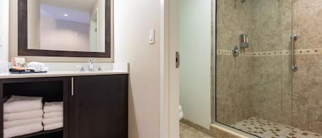 Un baño con tocador de madera oscura, un espejo grande y zona de ducha con puerta de vidrio.