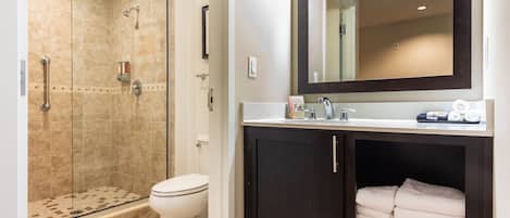 Une salle de bain avec une douche à parois de verre, des toilettes, un lavabo avec un miroir et un meuble contenant des serviettes.