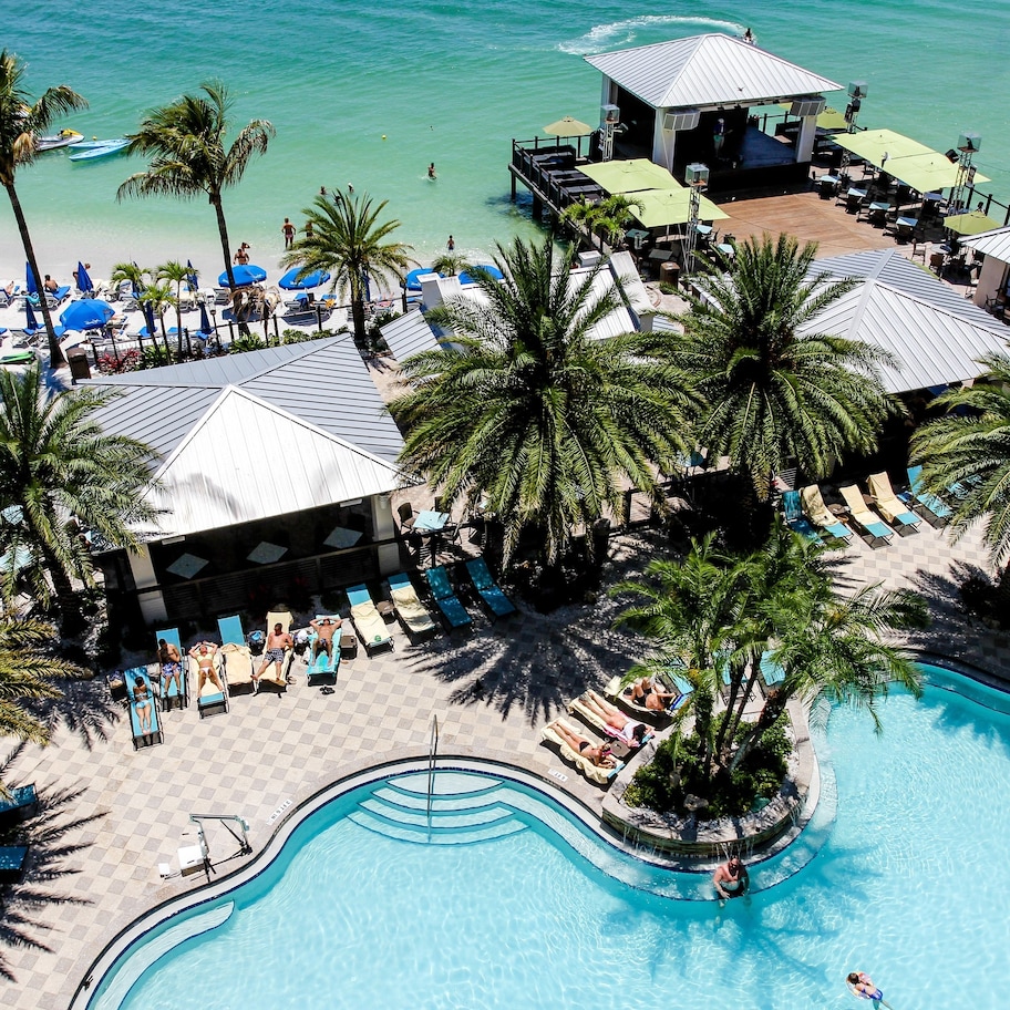 An aerial view of a resort with a swimming pool, beach area, and lounge chairs.