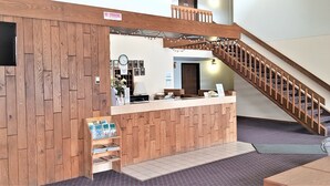 A reception area with a wooden counter, a clock, framed pictures, and a staircase. - AmeriVu Inn & Suites - Avon (Avon)