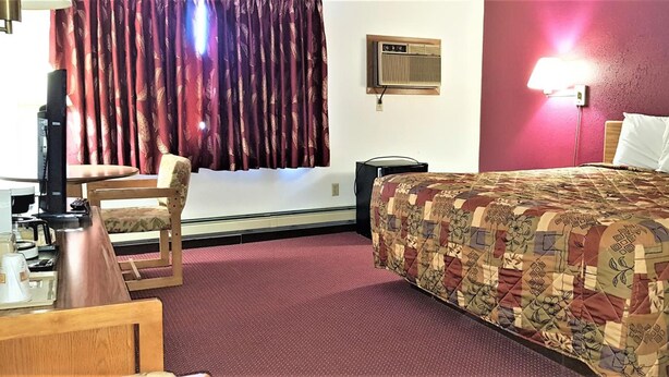 A hotel room with a bed, a desk, a chair, a lamp, and a window with curtains. - AmeriVu Inn & Suites - Avon (Avon)