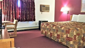 A hotel room with a bed, a desk, a chair, a lamp, and a window with curtains.