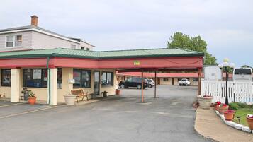 A motel with a red awning, a covered parking area, and several potted plants along the sidewalk.