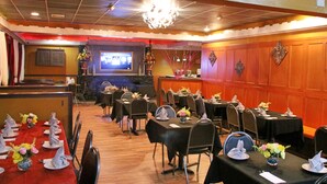 A restaurant with multiple tables set for dining, a bar area, and a television screen in the background. - Woodland Inn (Niagara Falls)