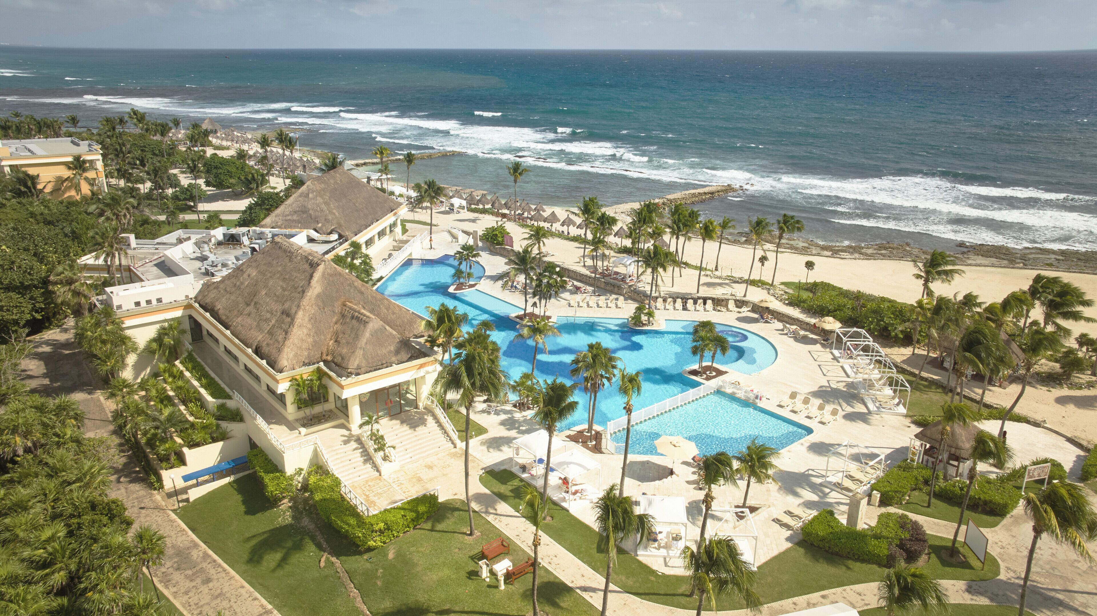 A resort with a large pool, palm trees, and a beach view.