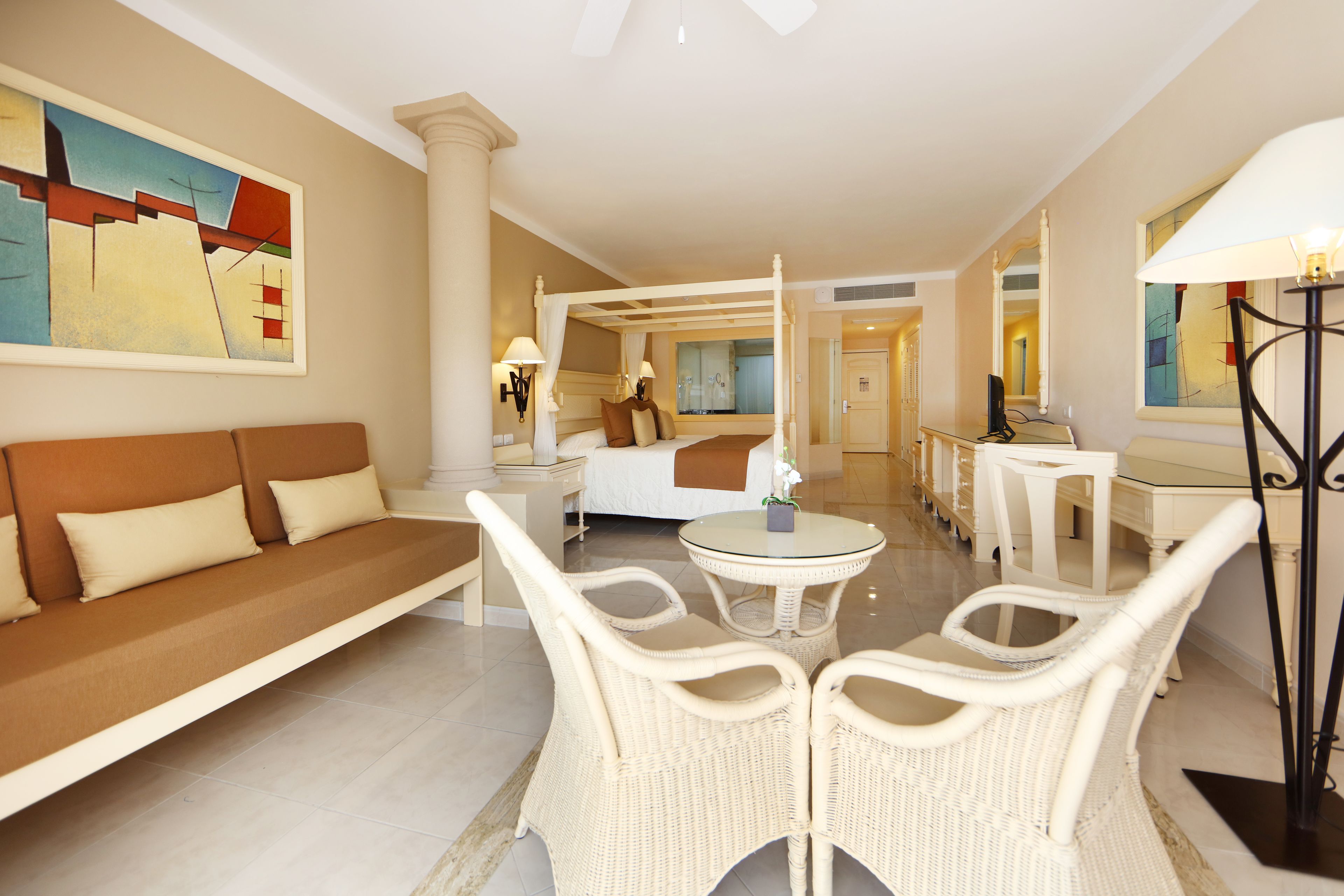 A hotel room with a large bed, a sofa, two chairs, a small table, and a lamp.