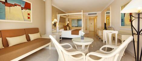 A hotel room with a large bed, a sofa, two chairs, a small table, and a lamp.