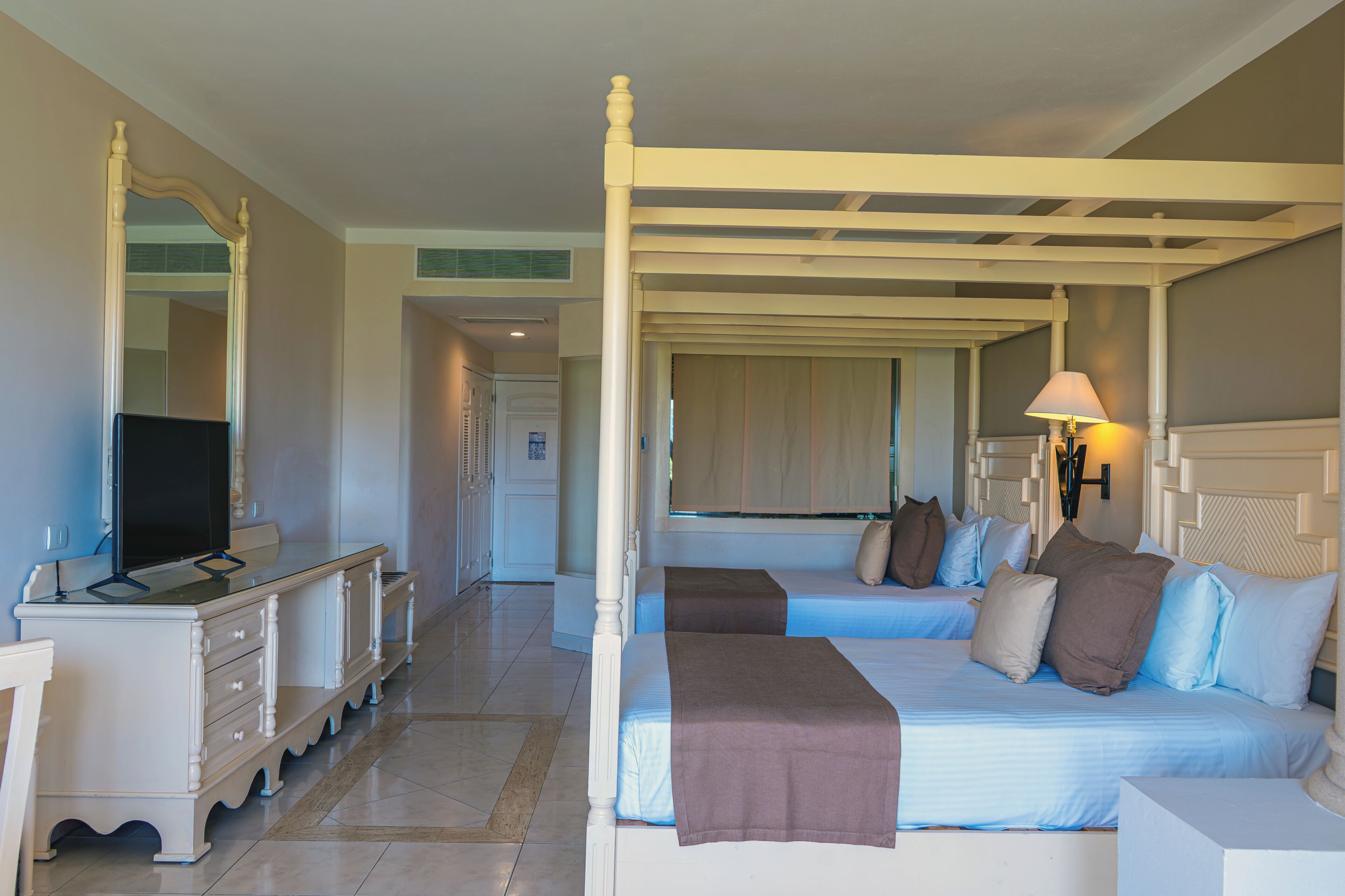 A four-poster bed with a headboard, two bedside tables, a television, and a lamp.