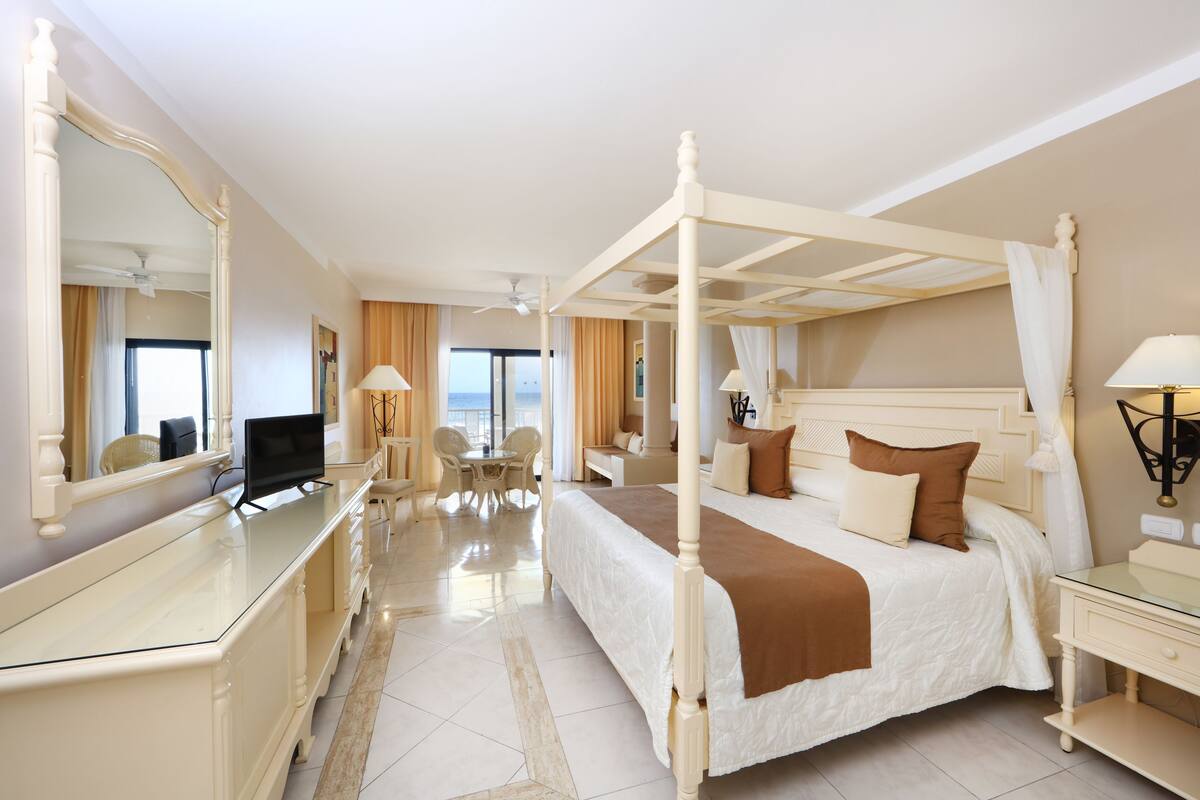 A four-poster bed with a television, a desk, and a chair in a hotel room.