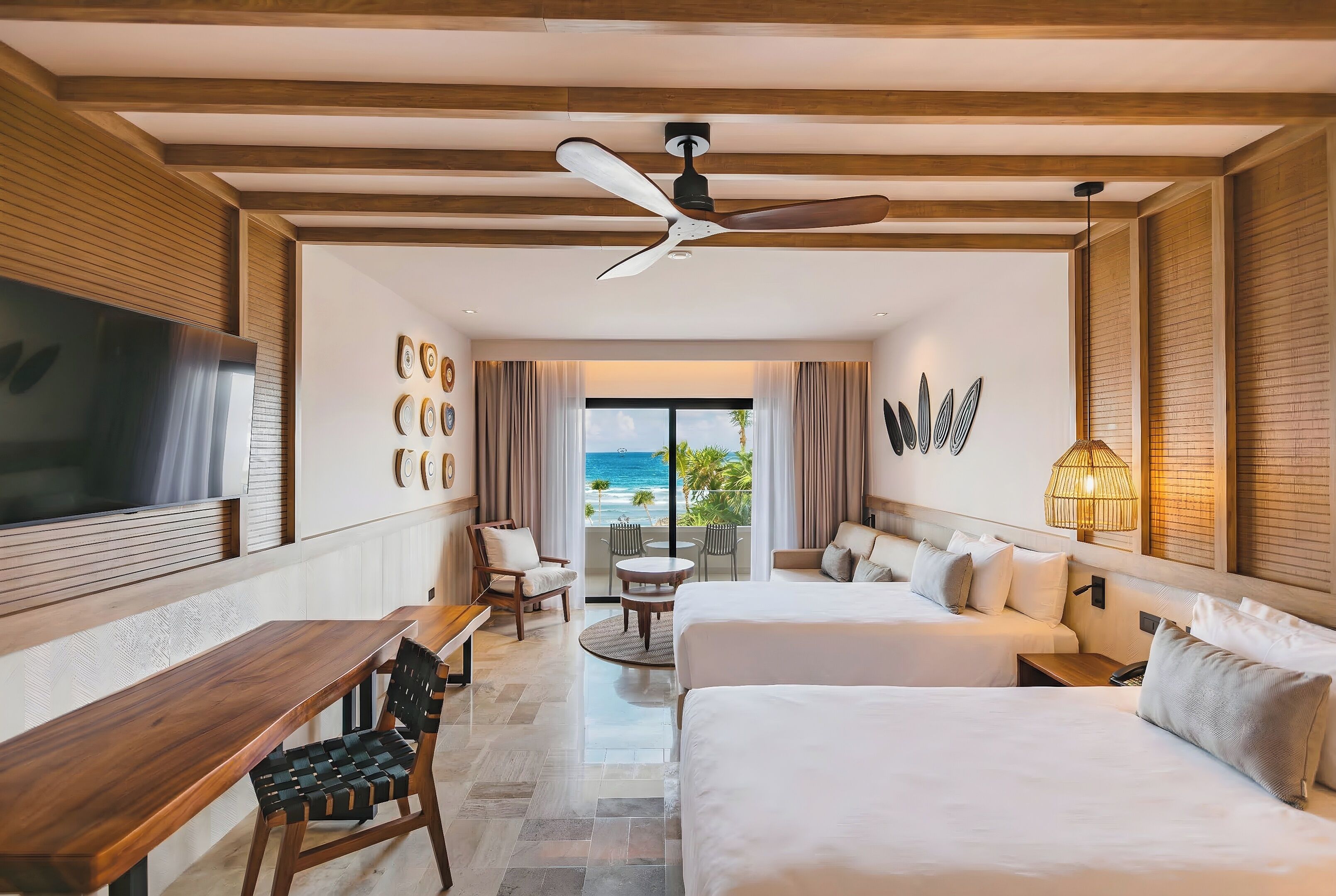 Habitación de hotel con una cama grande, un escritorio, una silla, un televisor y un balcón con vista al océano.