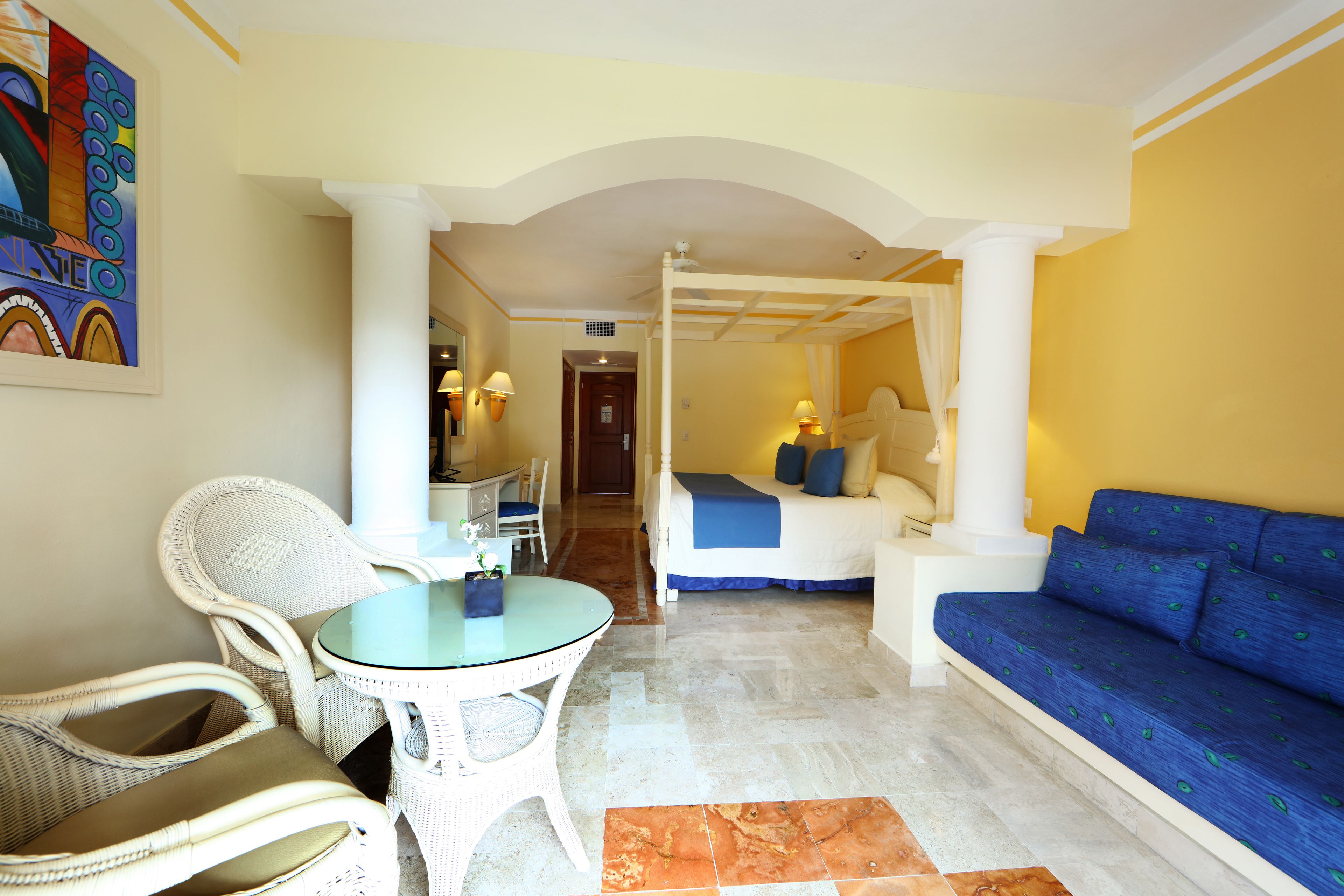 A room with a bed, a blue sofa, a dining table with chairs, and a small white table.