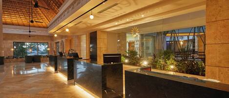 A spacious lobby with a high ceiling, a reception desk, and a large window offering a view of the outdoors.