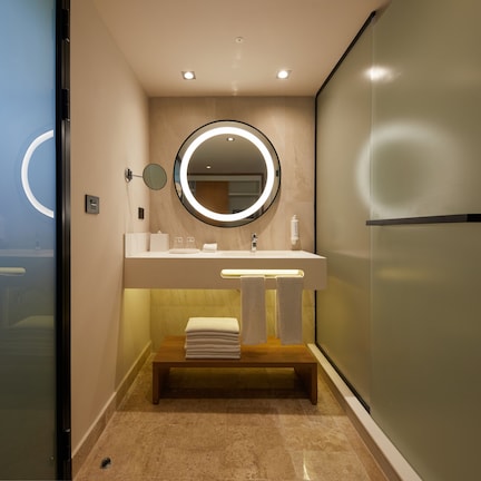 A modern bathroom with a round mirror, a sink, and a bench with towels.