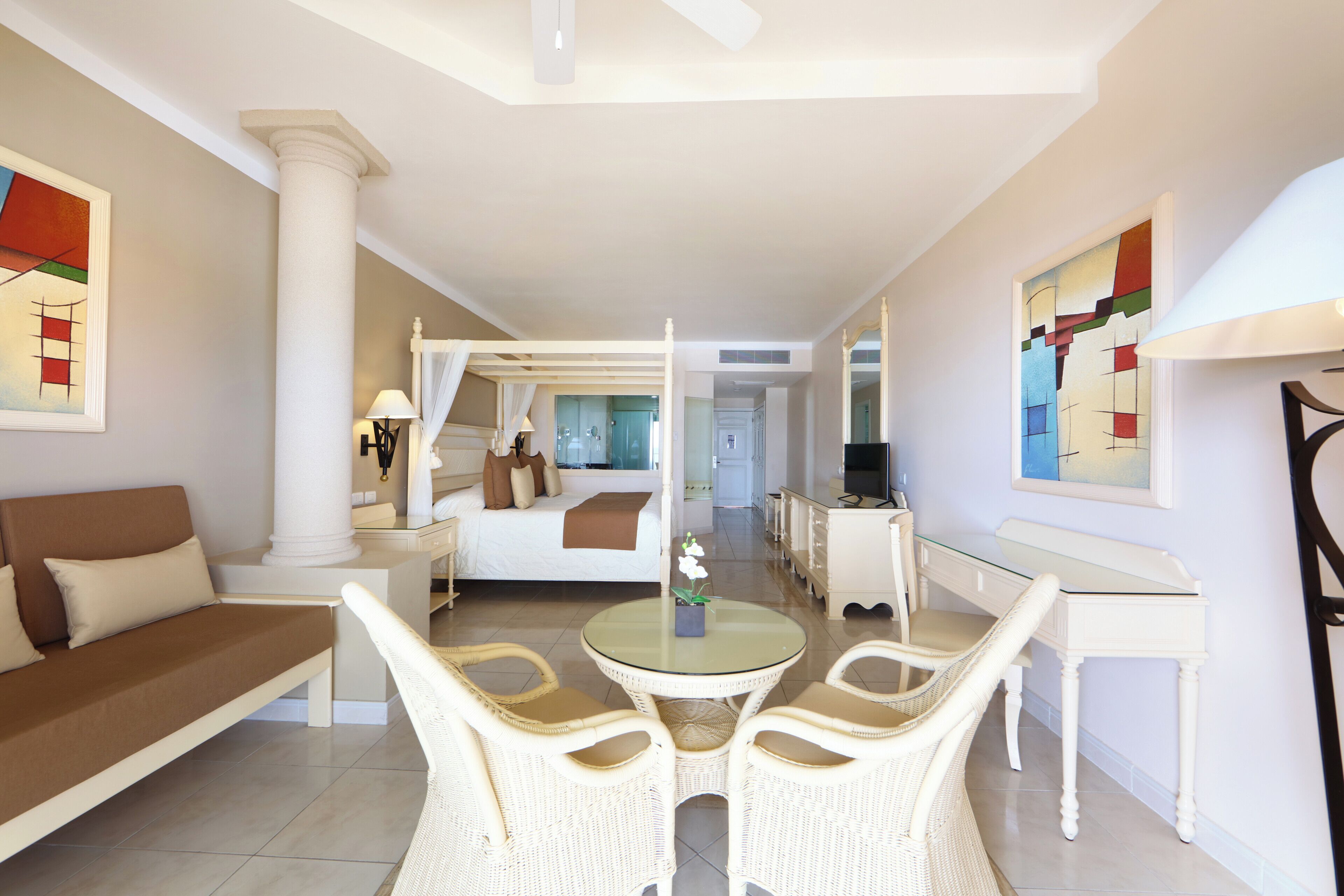 A hotel room with a bed, a sitting area with a sofa and chairs, a dining table, and artwork on the walls.