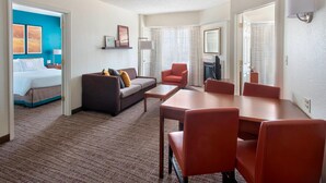 A hotel room with a bed, a sofa, a dining table with chairs, a TV, and a fireplace.