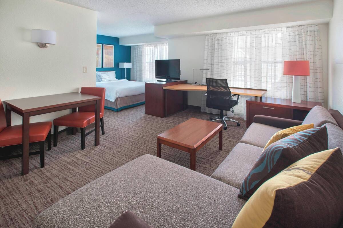 Una habitación de hotel con cama, escritorio, silla, sofá y televisor.