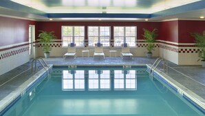 An indoor swimming pool with clear water, surrounded by red and white tiled walls, and equipped with sun loungers and potted plants.