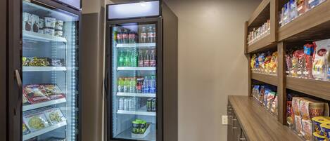 A kitchenette area with two refrigerators stocked with beverages and snacks, and shelves with packaged food items.