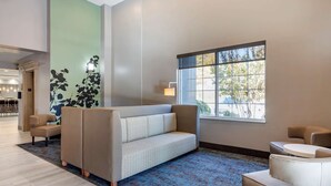 A modern lobby with a sofa, armchairs, a patterned rug, and a large window with a view of trees. - Sleep Inn & Suites Lebanon - Nashville Area (Lebanon)