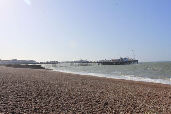 A pebbled beach with a pier extending into the sea.