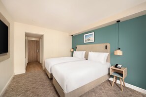 A hotel room with two beds, a small bedside table with a phone, a wall-mounted picture, and a door leading to another room. - The Old Ship Hotel (Brighton)