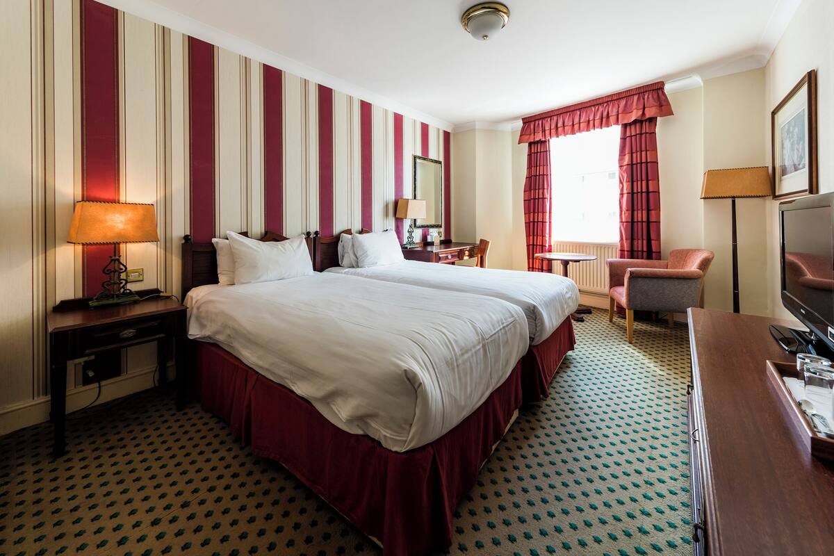 A hotel room with two beds, a desk, a chair, a television, and a window with curtains.