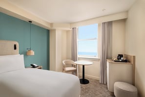A hotel room with a bed, a desk with a phone, a chair, a small table, a coffee machine, and a view of the sea. - The Old Ship Hotel (Brighton)
